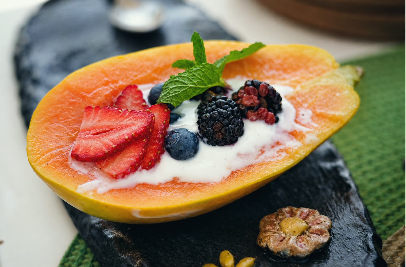 Papaya servida con yogur y frutos rojos sobre pizarra oscura