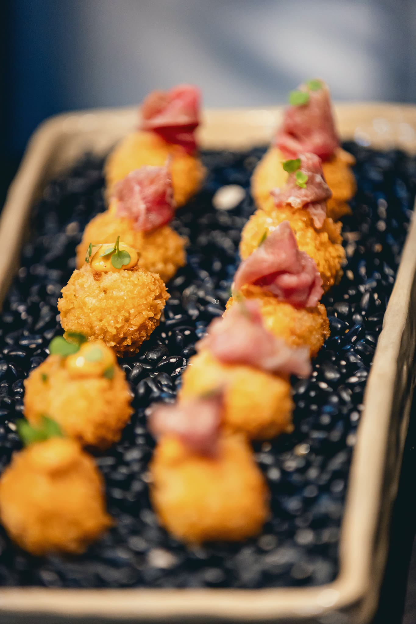 Golden croquettes with slices of ham, on black grains