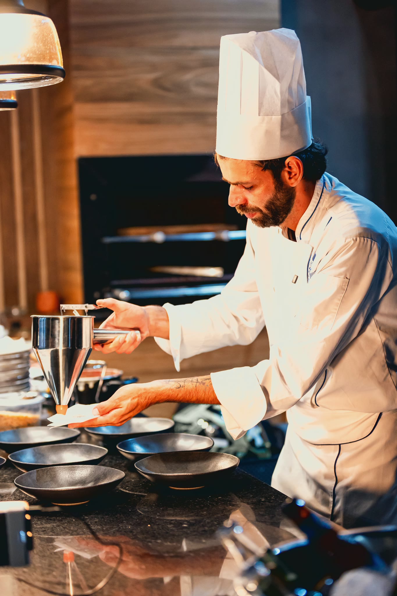 Chef Vitor Jover plating at the counter, under the pendant lights