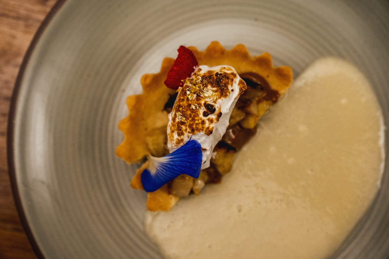 Dessert with a blue flower and cream on the side, on a grey plate