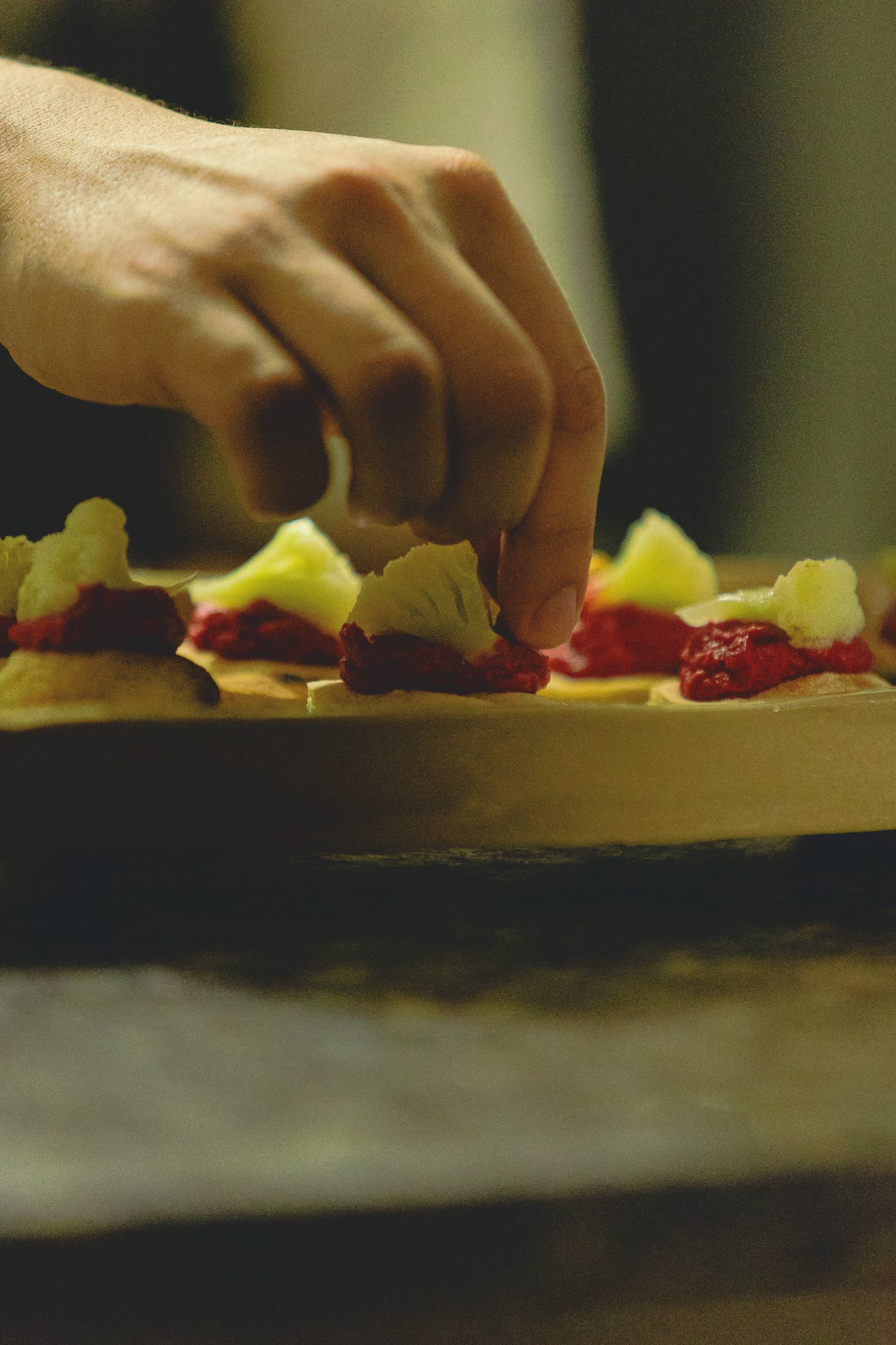 Mão finalizando canapés sobre uma tábua de madeira