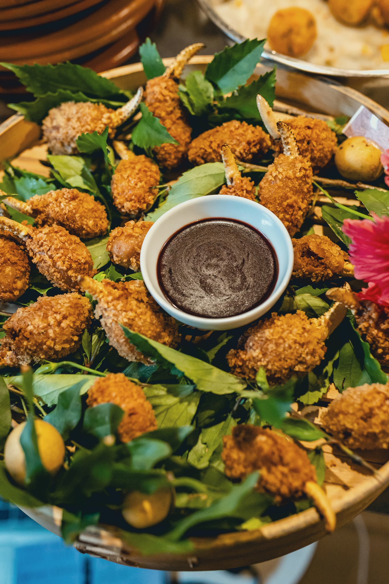 Breaded fritters on leaves, with a bowl of dark sauce in the centre