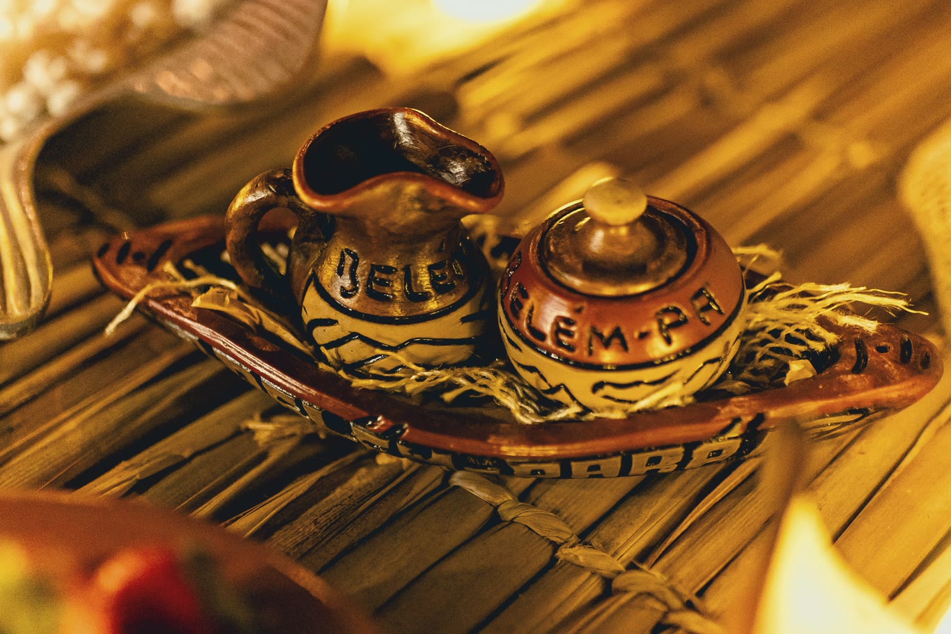 Ceramic pieces marked “Belém-PA” on a straw mat, by candlelight