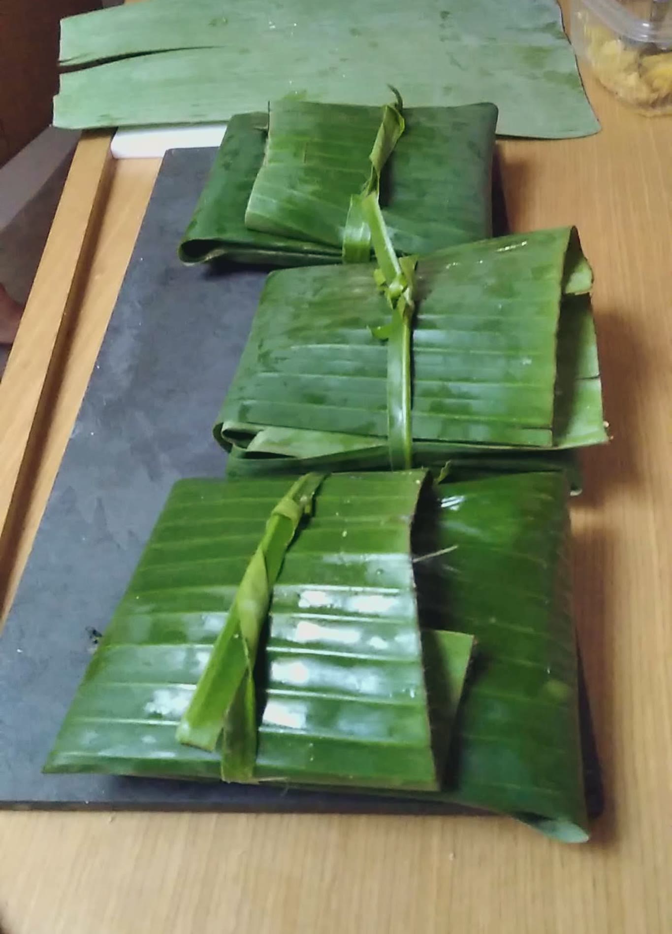 Trouxinhas de folha de bananeira amarradas, enfileiradas sobre uma lousa